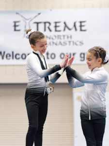 thrive gymnastics aurora ontario gymnasts high five with medal at competition