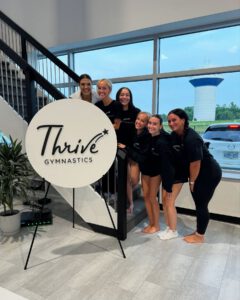 thrive gymnastics aurora ontario staff team pose with logo sign